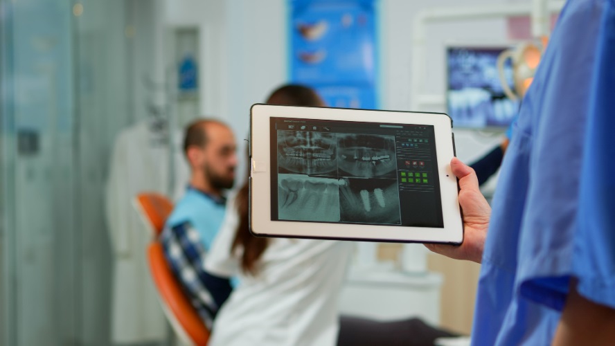 close-up-dentist-nurse-holding-tablet-with-digital-radiography-while-doctor-is-working-with-patient-background-examining-teeth-problem-sitting-stomatological-chair-dental-clinic500